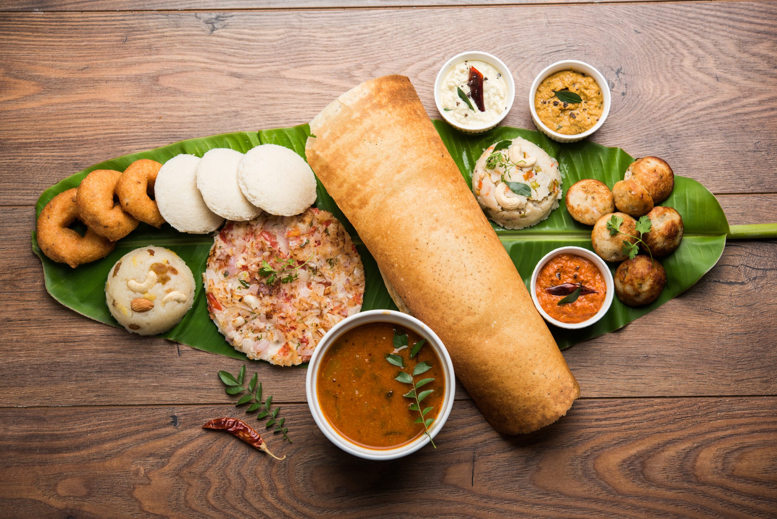 Group of South Indian food like Masala Dosa, Uttapam, Idli or idly, Wada or vada, sambar, appam, semolina halwa, upma served over banana leaf with colourful chutneys, selective focus Group of South Indian food like Masala Dosa, Uttapam, Idli or idly, Wada or vada, sambar, appam, semolina halwa, upma served over banana leaf with colourful chutneys, selective focus
